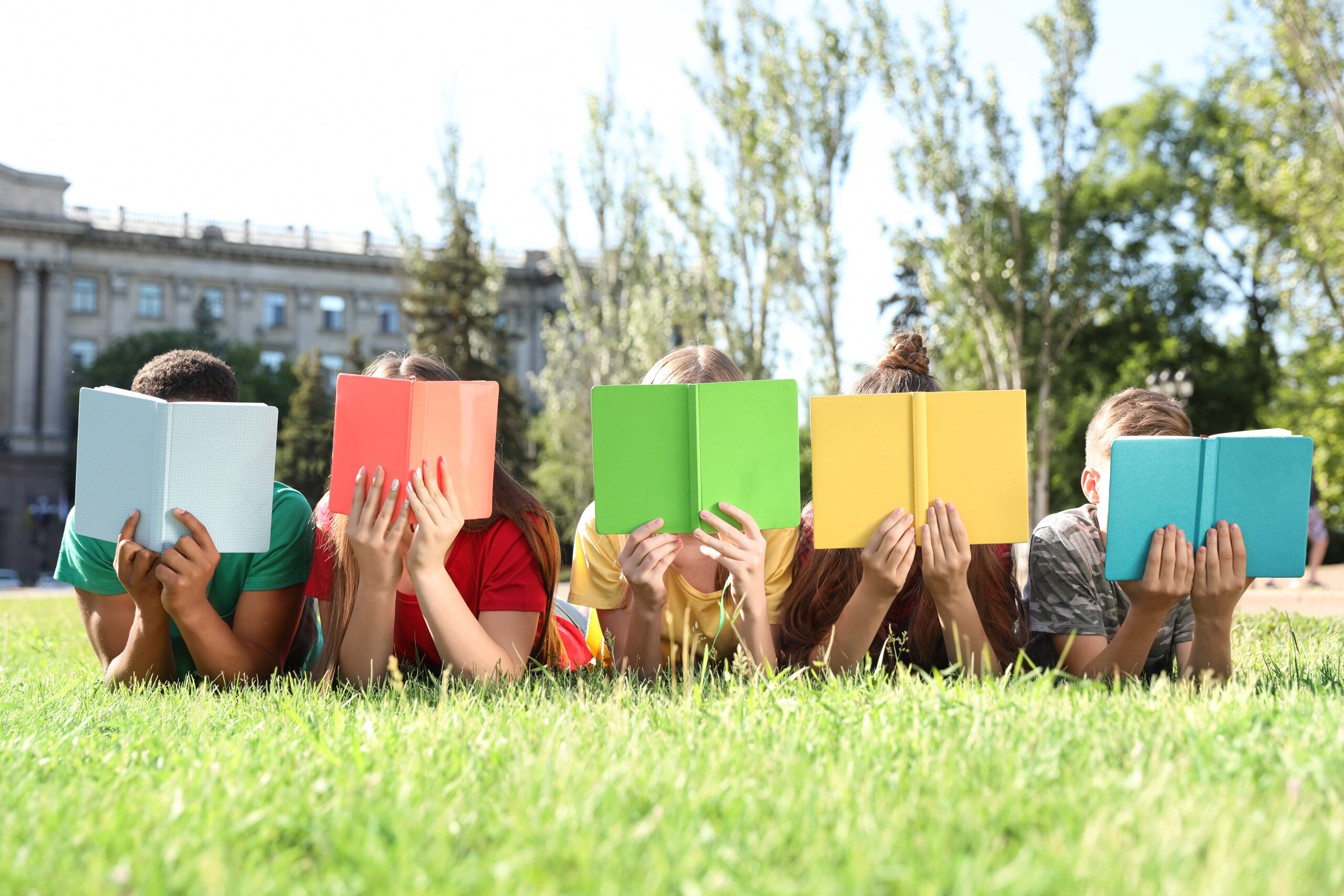 children lying on grass holding books in front of their faces