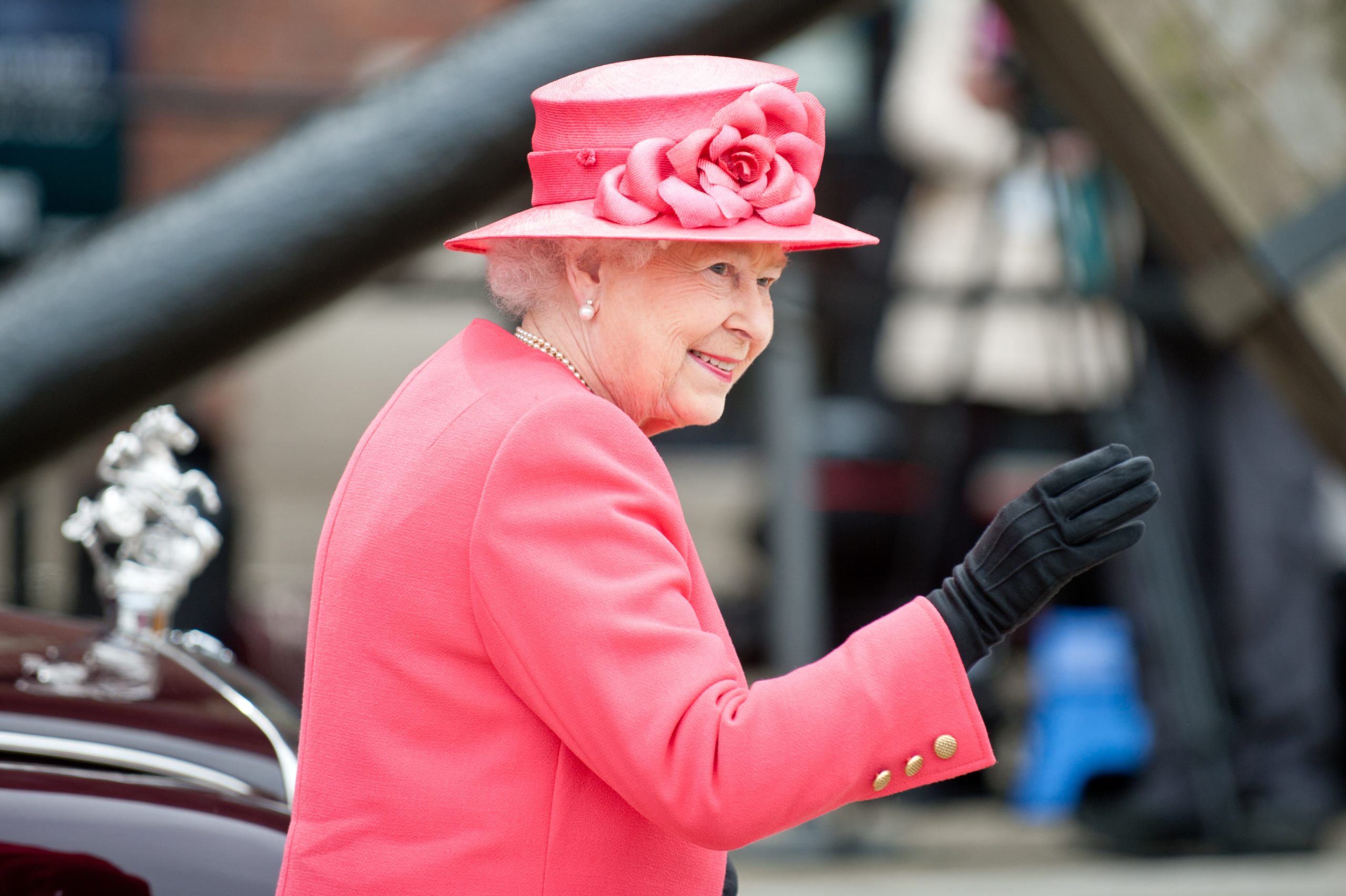 Queen Elizabeth II waving in a fuchsia pink hat and suit