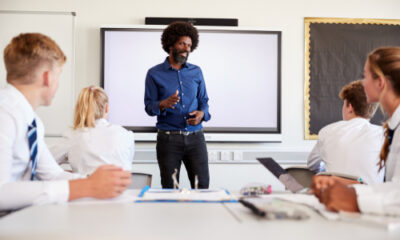 Male teacher standing in front of whiteboard talking to pupils