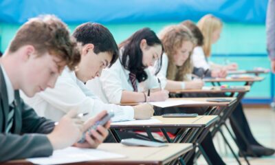 a row of school students writing and using a calculator in an exam