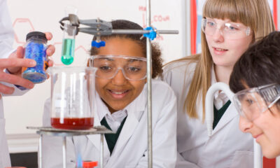 Two female students looking at a beaker with a red liquid in it, wearing lab coats