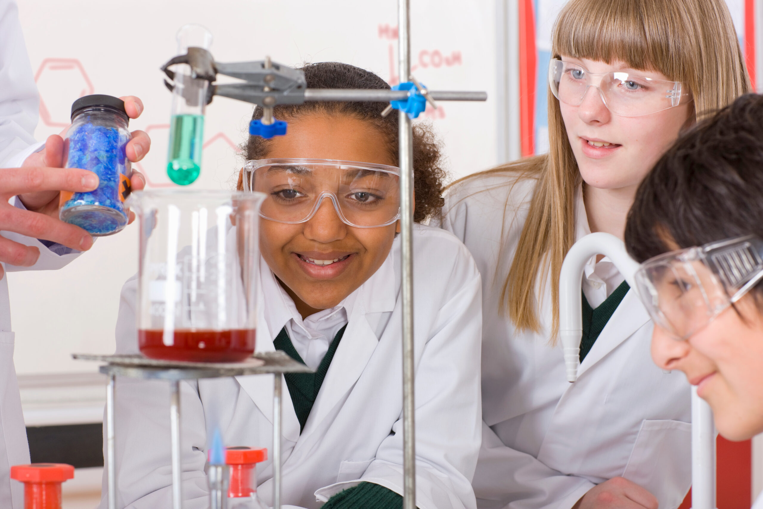 Two female students looking at a beaker with a red liquid in it, wearing lab coats