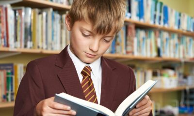Boy wearing school uniform reading book in library