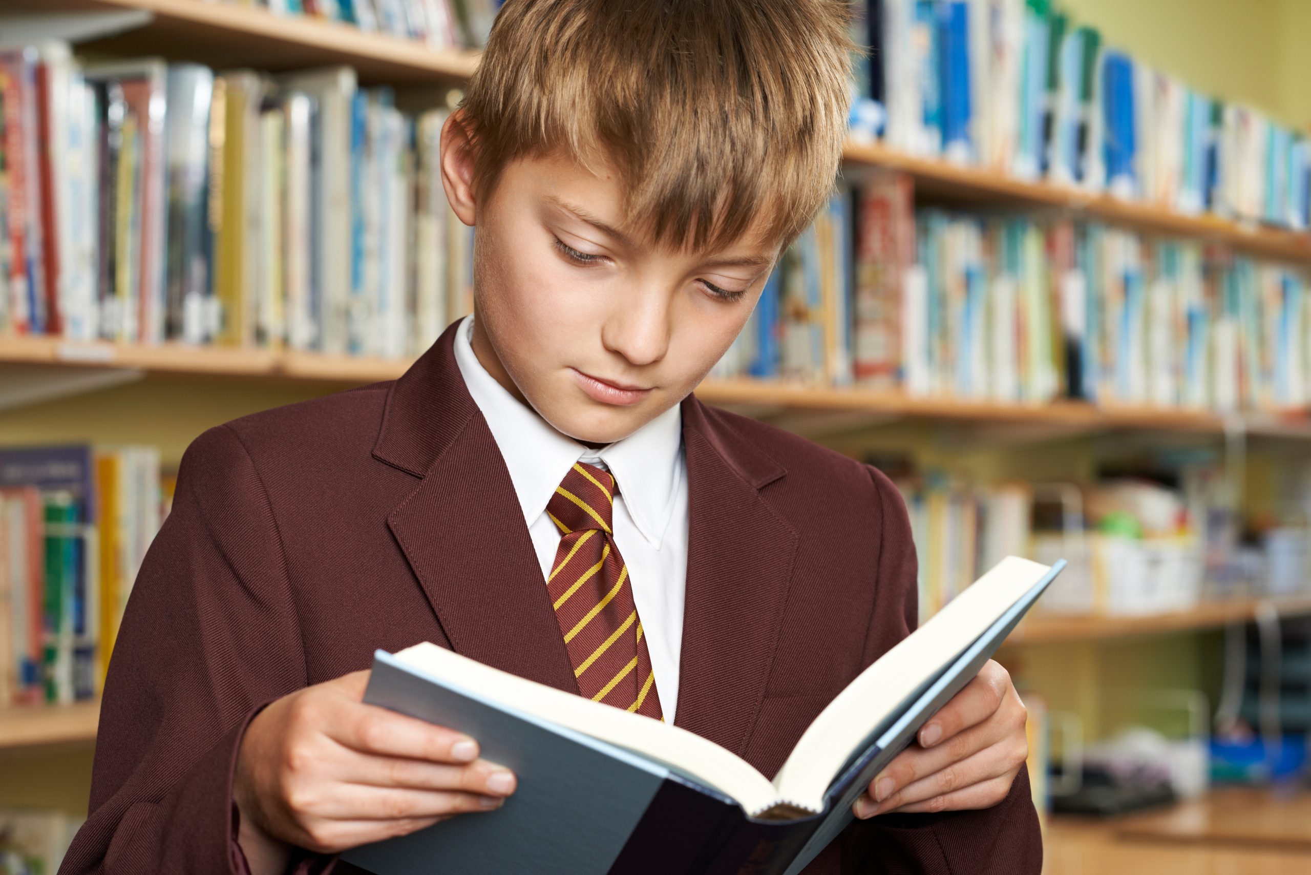 Boy wearing school uniform reading book in library