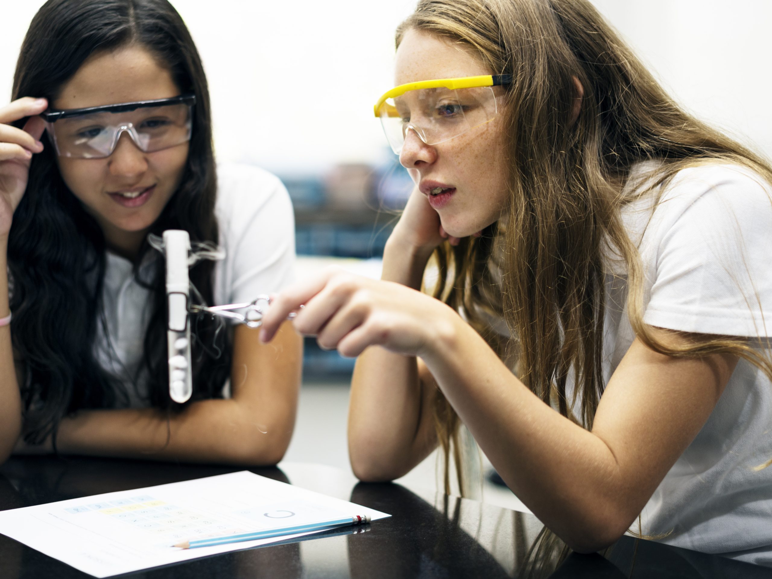 female students in science classroom wearing goggles and holding a test tube